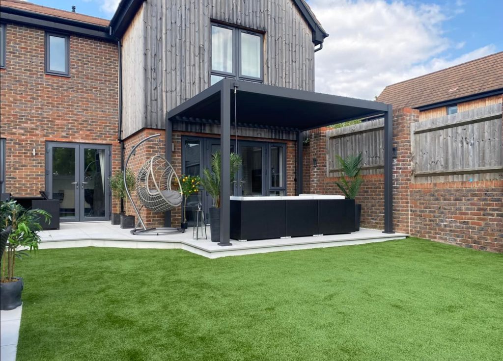 A brick house with black gazebo, outdoor seating and artificial grass installation
